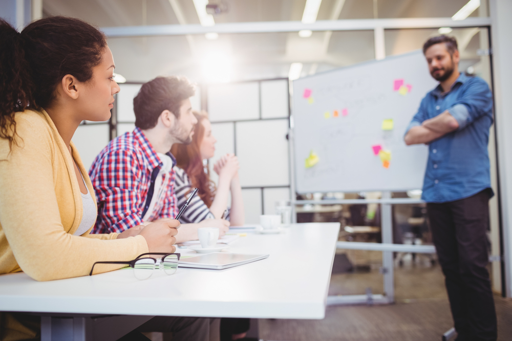 Male executive standing in front of colleagues during braintstorming in meeting room at creative office